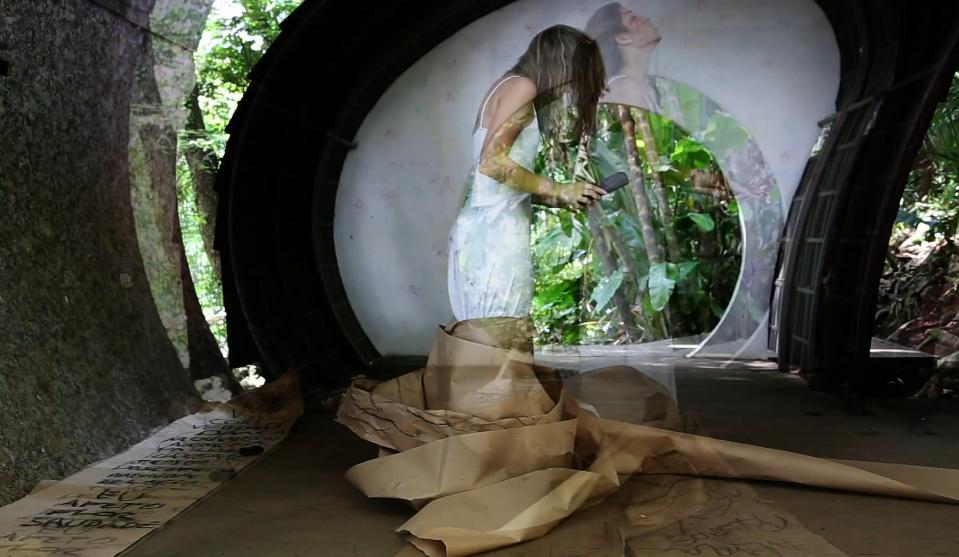 Performance com projeção de imagens, papéis e escrita no chão em meio à mata