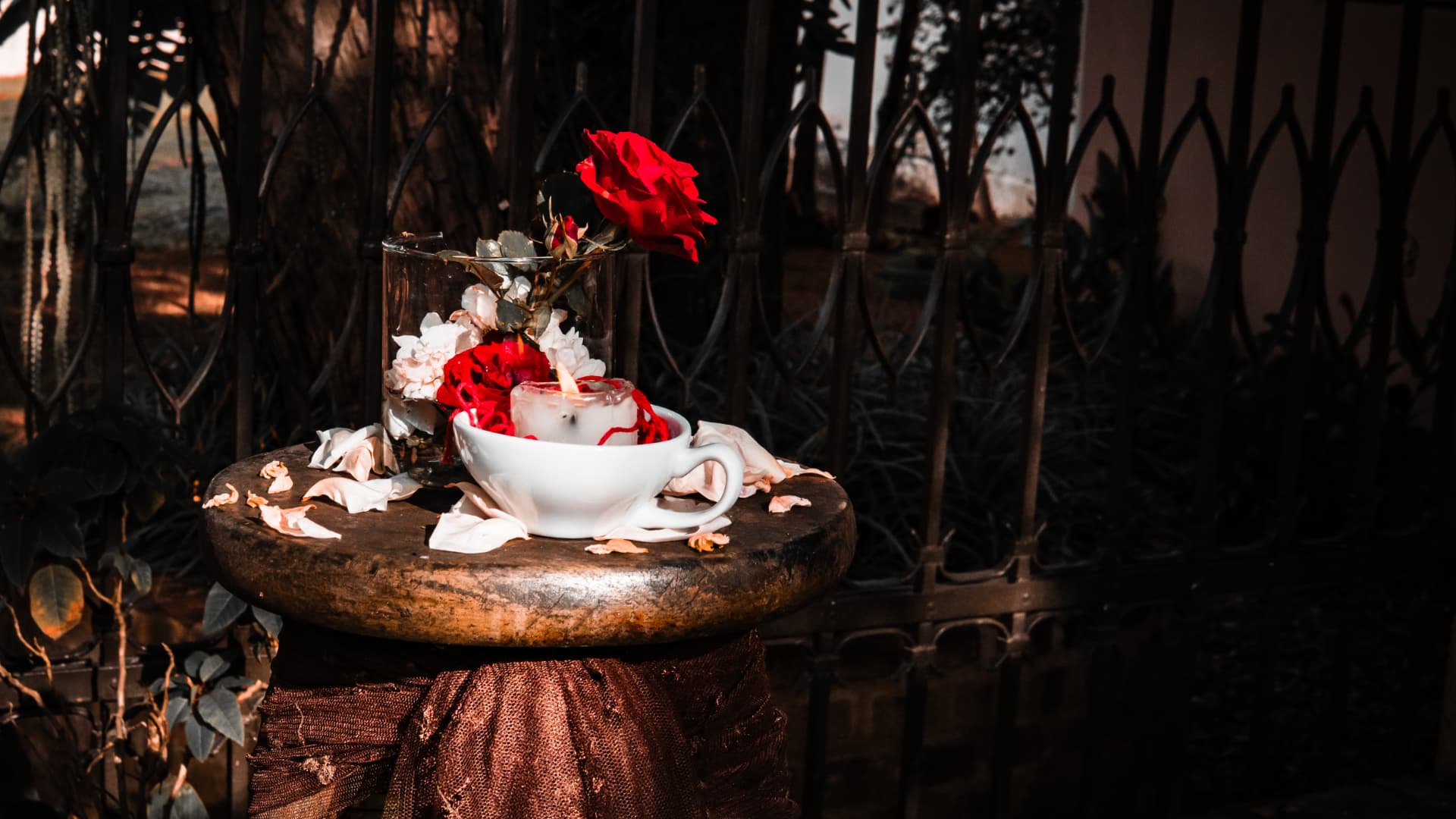 Pequeno altar com vela acesa, rosa vermelha e pétalas sobre banqueta de madeira